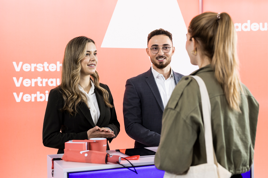 Auf einer Jobmesse unterhält sich eine Studentin mit Amadeus Fire Mitarbeitern am Messestand